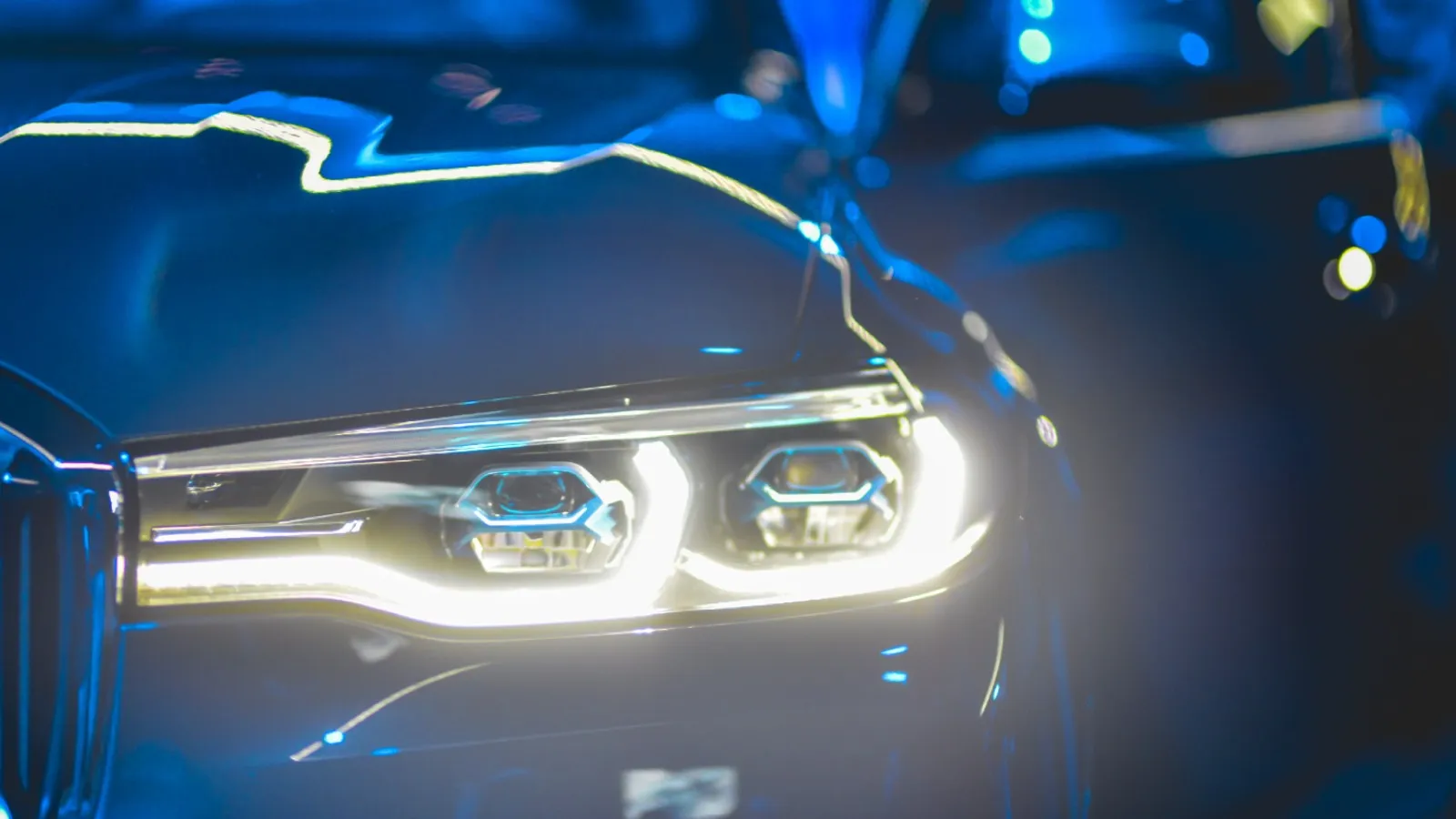 Primer plano de un faro de coche con luces LED brillantes en un entorno nocturno de tonos azules.